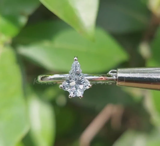 Engagement ring video with white metal band, kite-shaped clear center stone in prong setting, front view against green leaves

