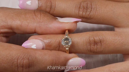 Engagement ring with rectangular clear gemstone, yellow metal band, halo design with round accent stones, worn on finger, front view
