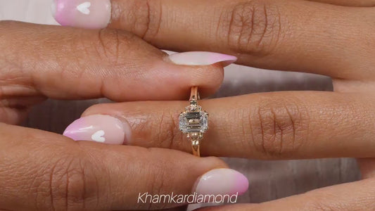 Engagement ring with rectangular clear gemstone, yellow metal band, halo design with round accent stones, worn on finger, front view
