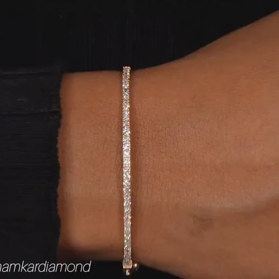 Bracelet with yellow metal band, round stones in a slim tennis bracelet design, worn on a wrist, close-up top view
