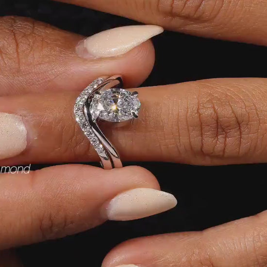 Engagement ring set with oval solitaire diamond and curved pavé wedding band worn on a hand, close-up view